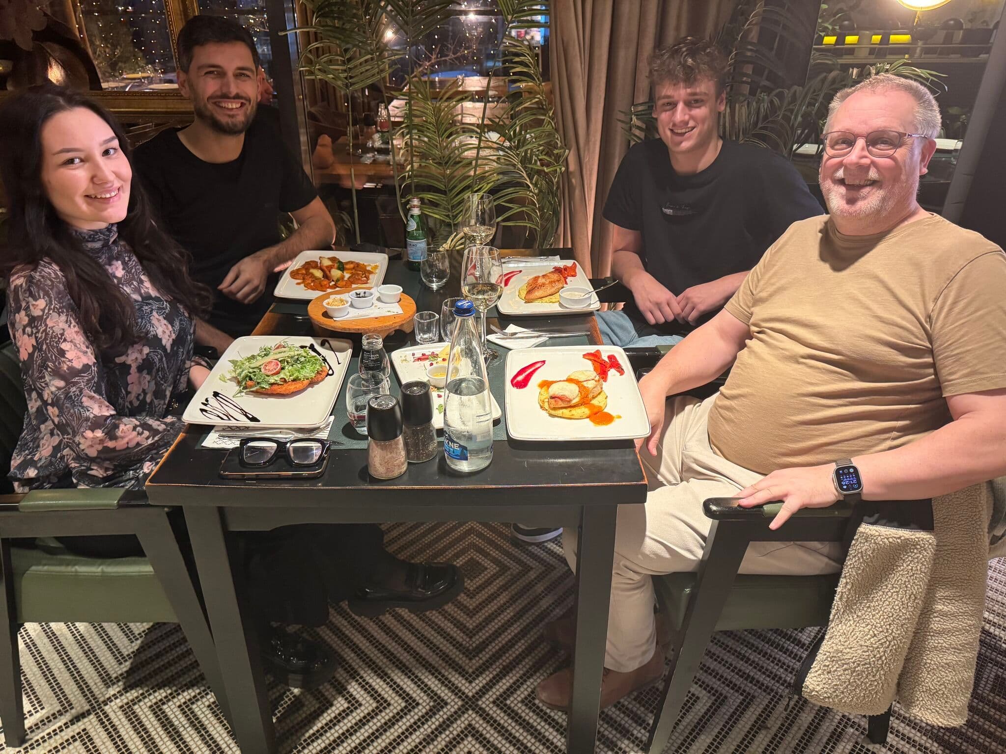 Four friends smiling and enjoying dinner together at a restaurant.